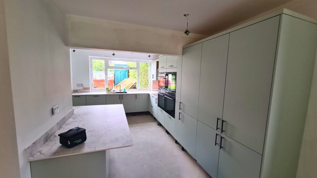 Before renovation view from the lounge into a dated kitchen with inset oven, sink beneath window and tired finishes in St Albans